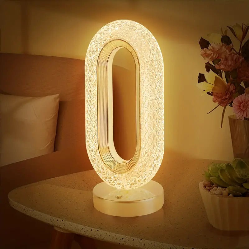 Decorative table lamp on a nightstand with a warm glow, surrounded by flowers and a plant.